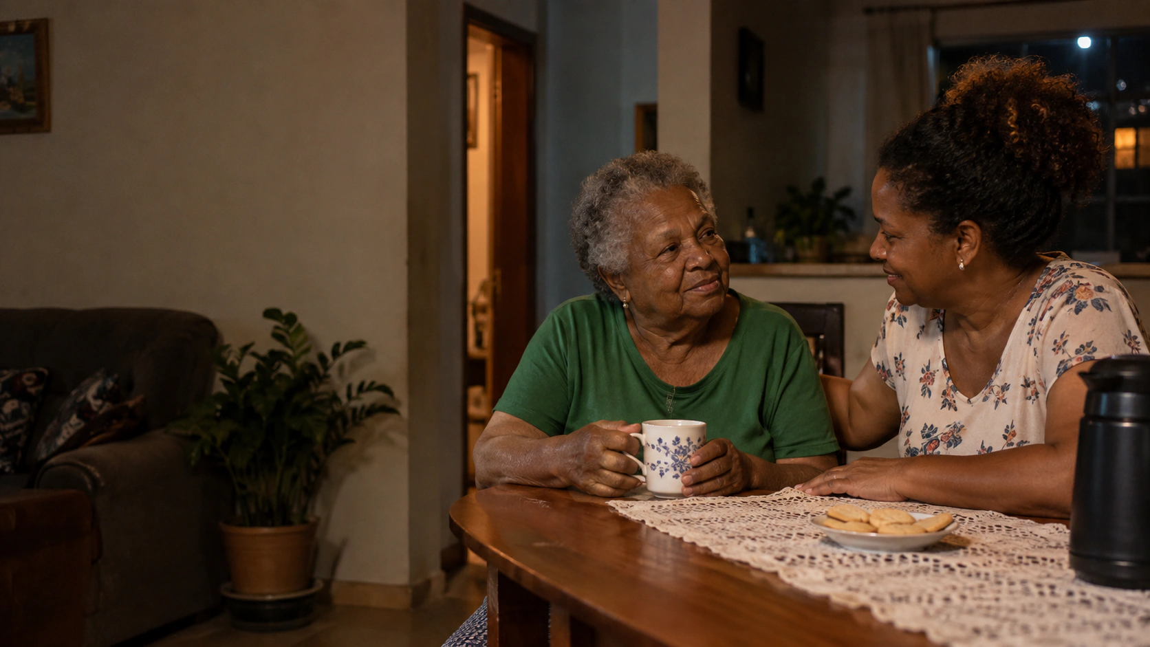 Mulher idosa conversando com uma familiar à mesa de casa.