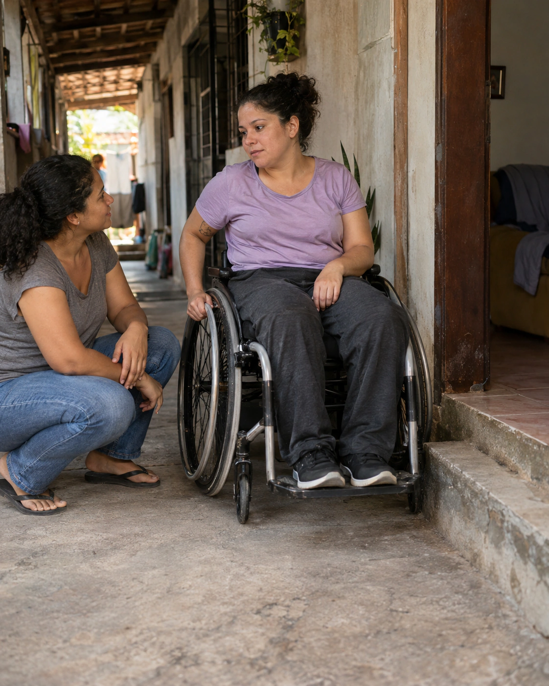 Mulher em cadeira de rodas junto a um degrau, com uma familiar ao lado.